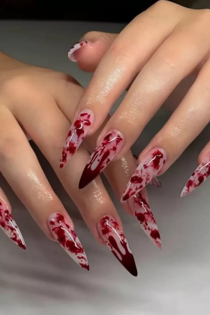 Long stiletto nails with a white base and a dark red "blood splatter" or ink-drop artistic design.