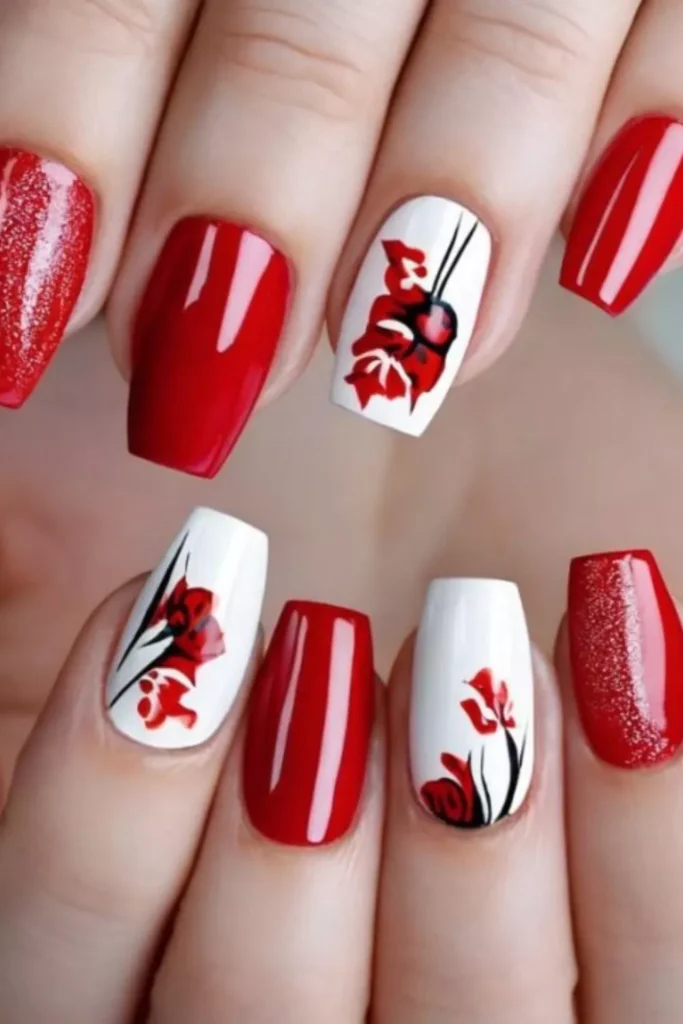 Medium length square nails featuring red polish and white accent nails with floral art.