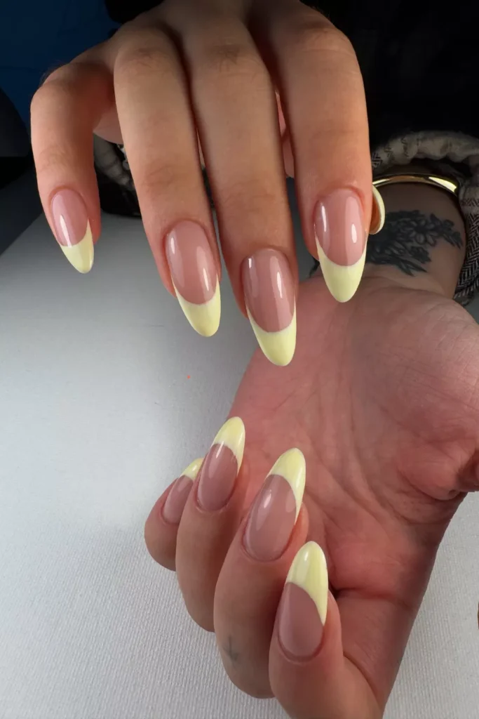 Long, almond-shaped nails featuring a high-shine nude base and thick, buttery yellow French tips.