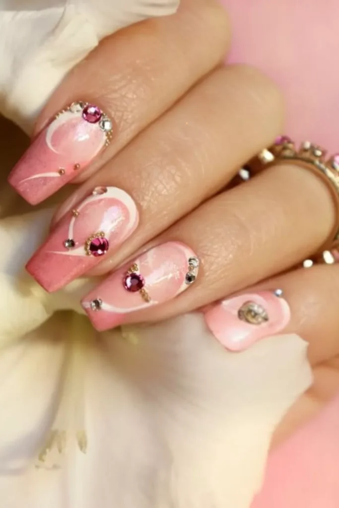 Long square-shaped nails featuring a pink marble and white swirl design, embellished with pink and clear rhinestones and delicate gold micro-beads.
