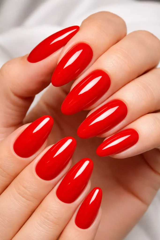 High-shine, vibrant cherry red almond-shaped nails shown in a close-up against a soft white background.