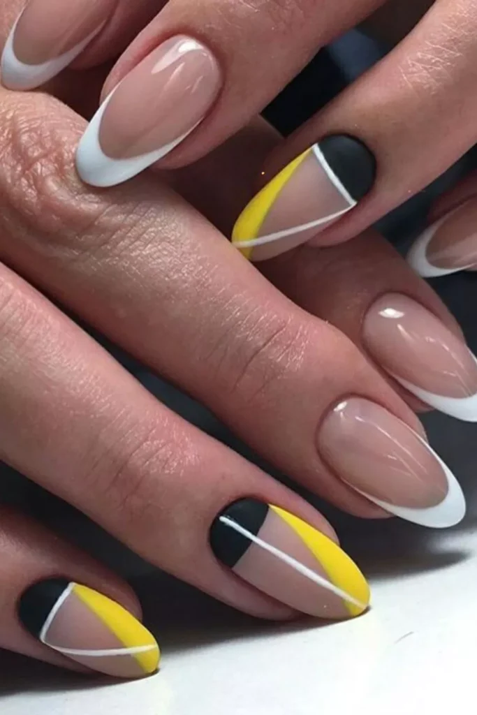 Close-up of almond-shaped nails featuring a mix of classic white French tips and geometric accent nails with matte black, yellow, and negative space sections divided by thin white lines.