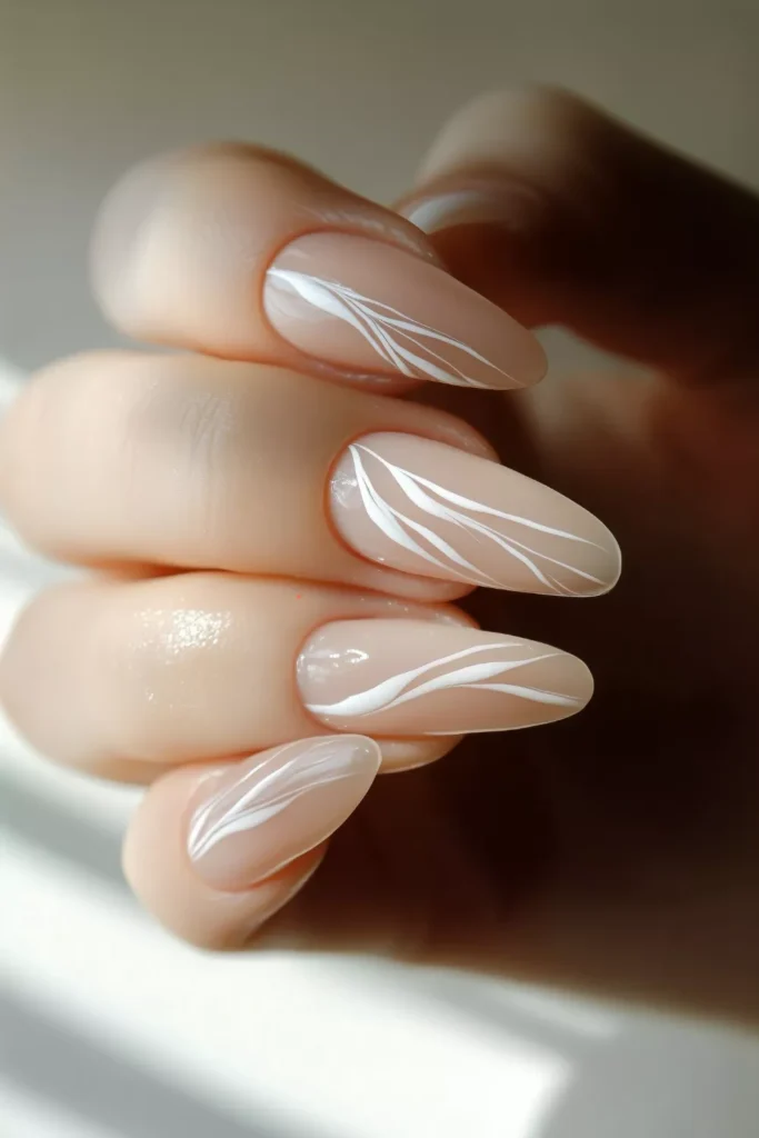 Long, almond-shaped glossy beige nails decorated with delicate, wispy white marble-style lines flowing across the surface of each nail.