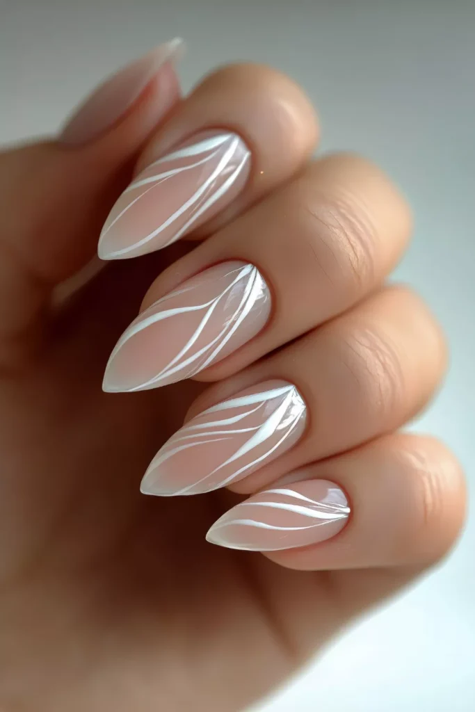 Long, pointed almond-shaped nails featuring a glossy nude base with elegant, flowing white abstract swirl patterns on each nail.