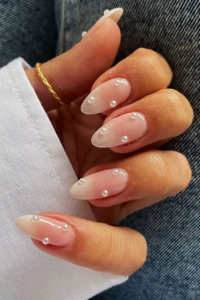 Long, almond-shaped nails with a glossy nude-to-white ombré base, featuring scattered 3D white pearl embellishments across each nail.