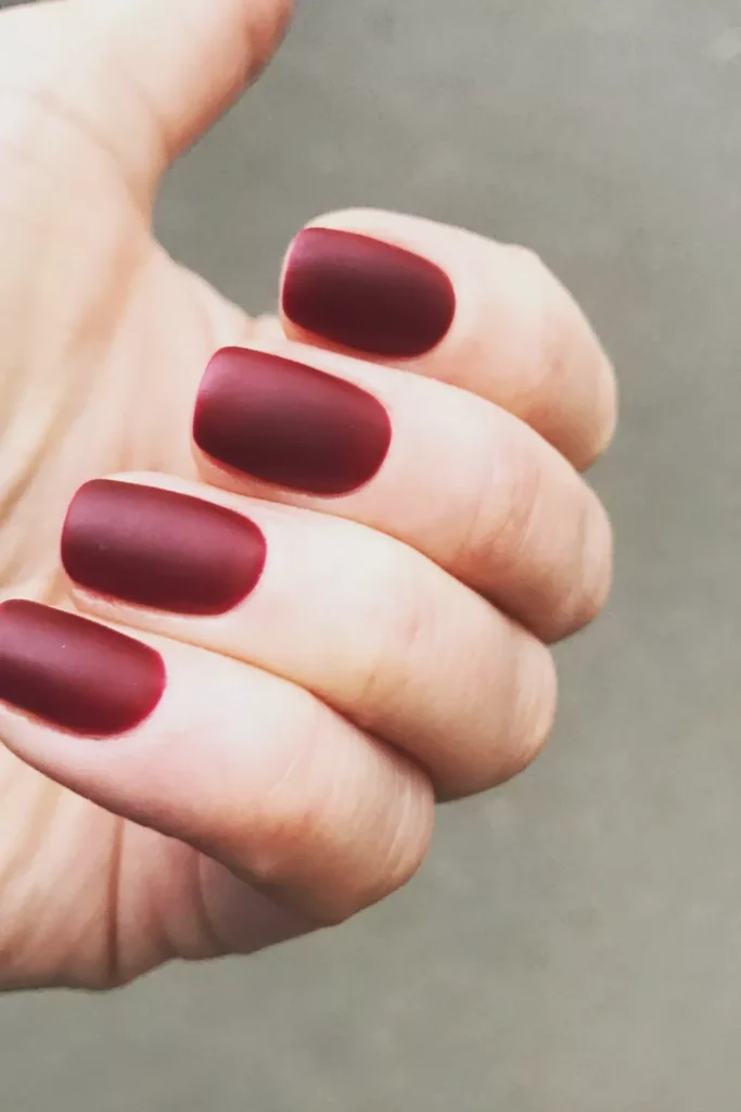 A hand featuring short, square nails painted in a smooth, velvet-finish matte burgundy wine color.