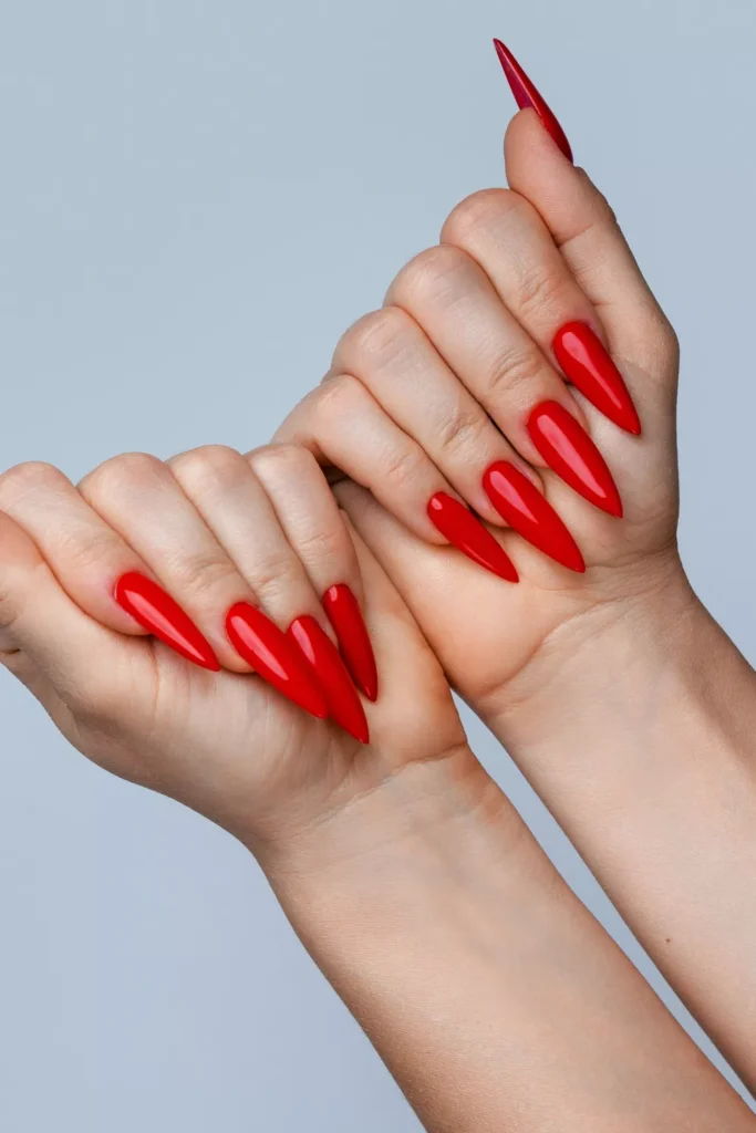 Very long pointed stiletto nails in a vibrant, glossy primary red shade.