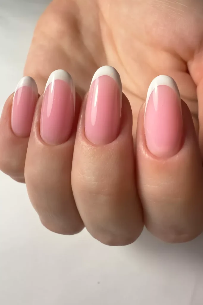 Close-up of glossy, medium-length oval nails featuring a classic pink base with thick, crisp white French tips.