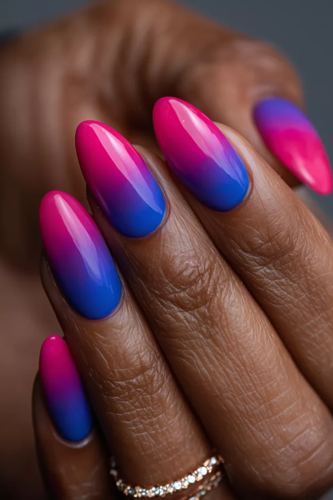 Long almond-shaped nails featuring a vibrant two-tone vertical ombre effect that transitions from a bright magenta pink on one side to a deep royal blue on the other.