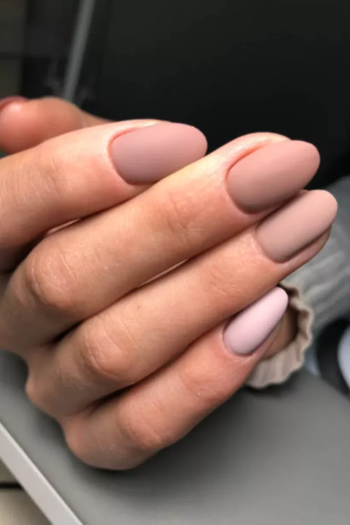 A close-up of a hand featuring oval-shaped nails with a smooth, velvety matte finish in a gradient of taupe, mauve, and soft pink tones.