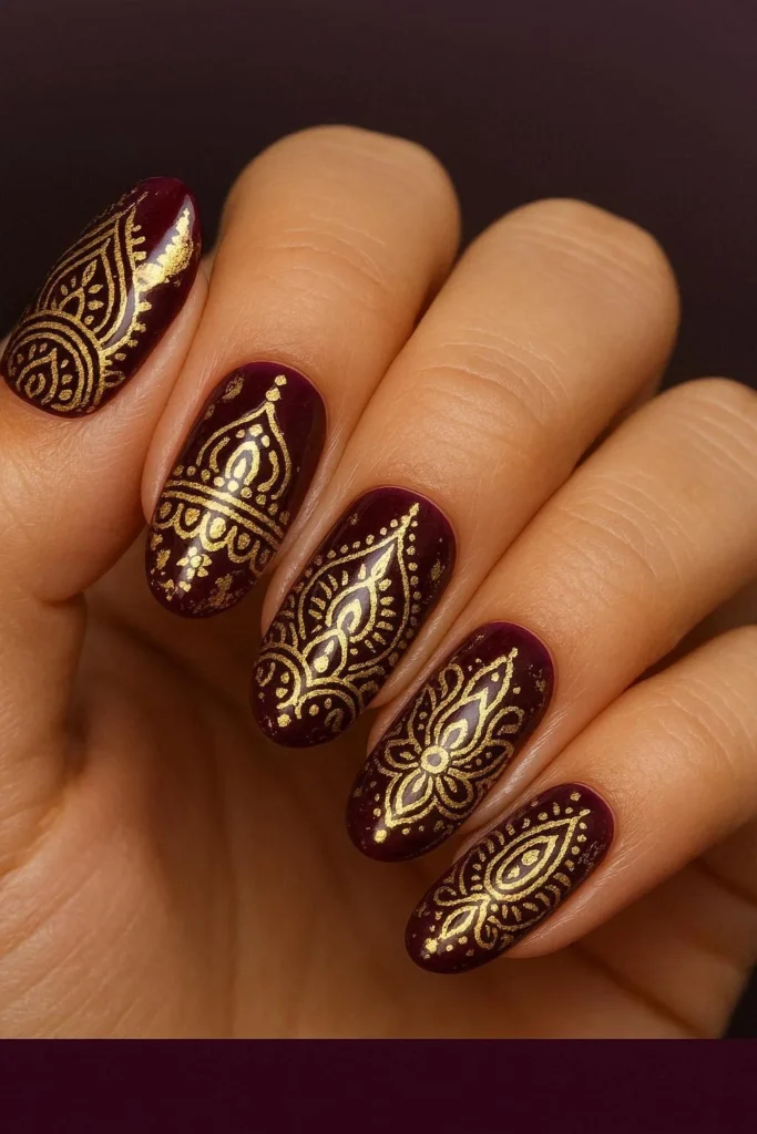 Long almond nails with deep plum base and intricate gold henna-inspired nail art for Diwali