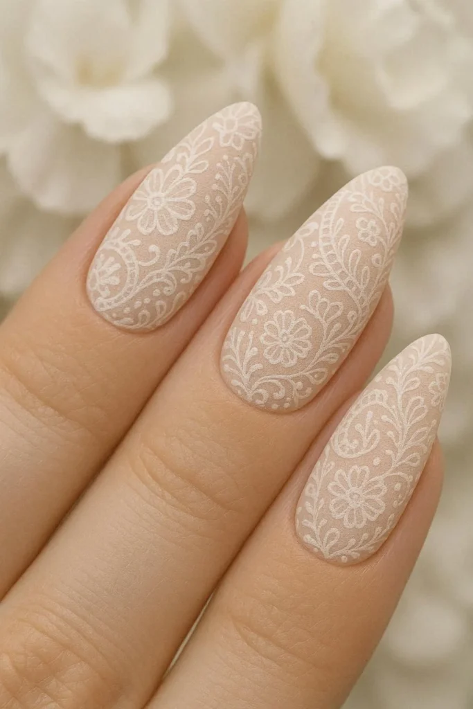 Long oval nails with nude blush base and intricate white lace nail art for Easter