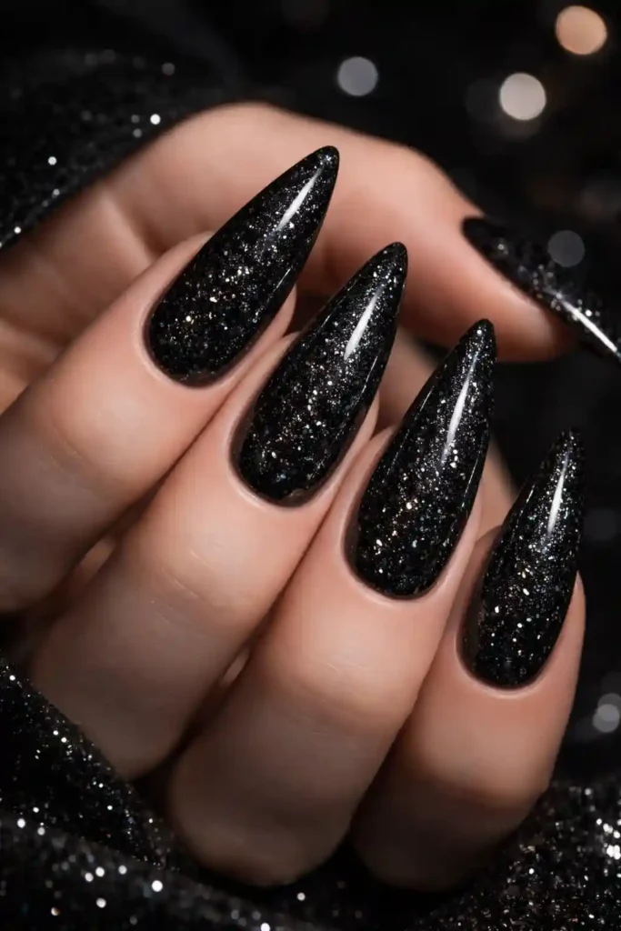 Black glitter nails with dense starlit sparkle on stiletto nails