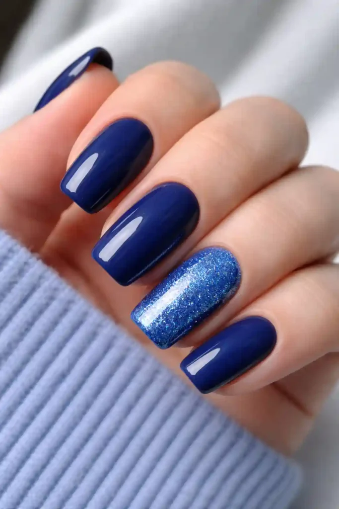 Blue glitter accent nail paired with solid navy nails on oval shape