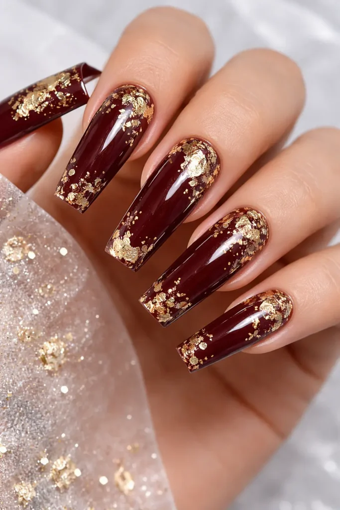 Burgundy nails with scattered gold foil flakes on coffin shape
