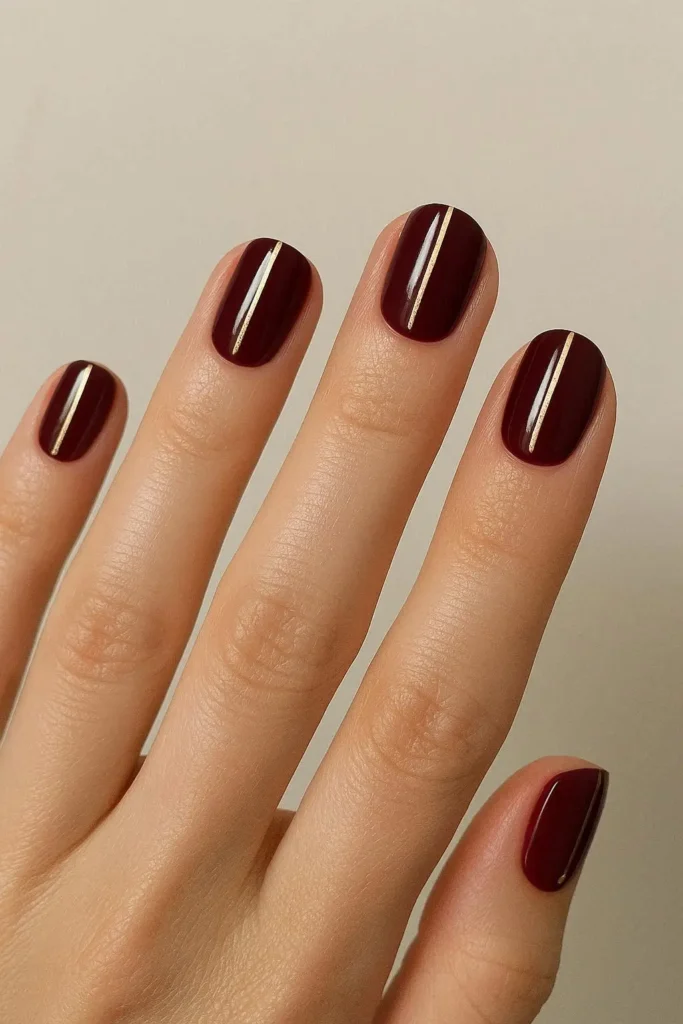 Burgundy minimalist nails with single gold line accent on short oval shape