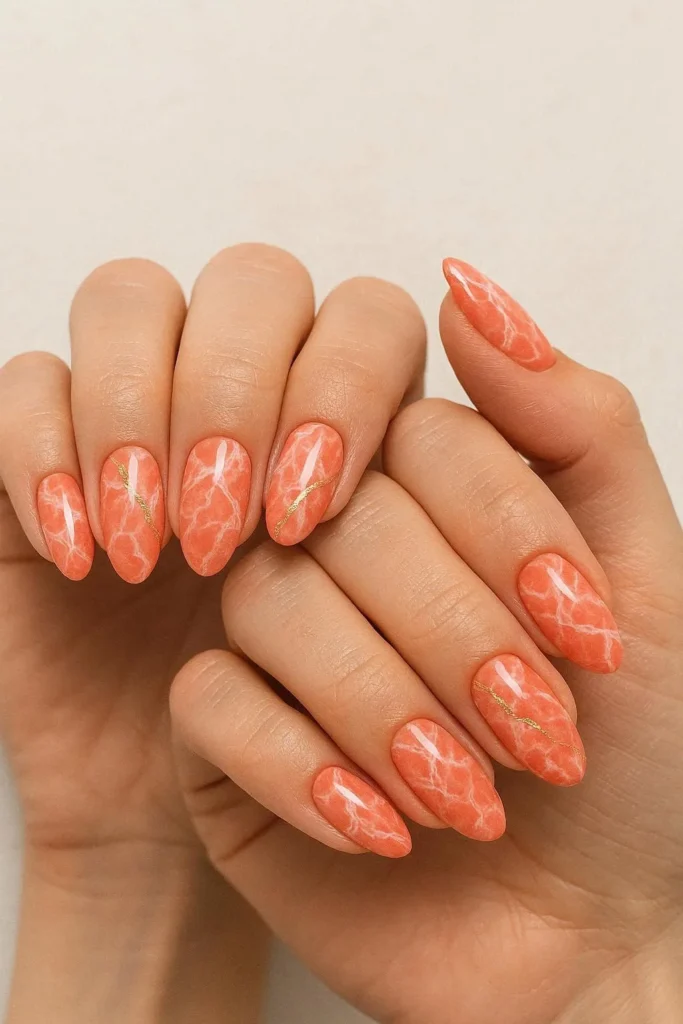 Coral marble nails with white and cream veining over a warm coral base resembling luxury stone