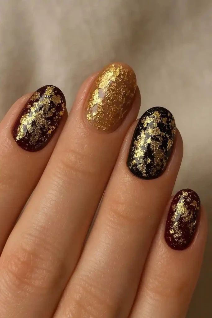 Gel nails with crinkled gold foil pressed into deep burgundy base
