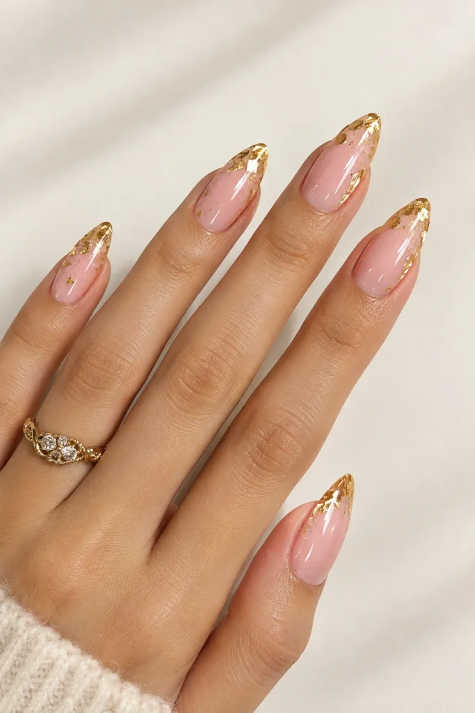 Pale pink almond nails decorated with marigold gold foil flakes and glossy polish