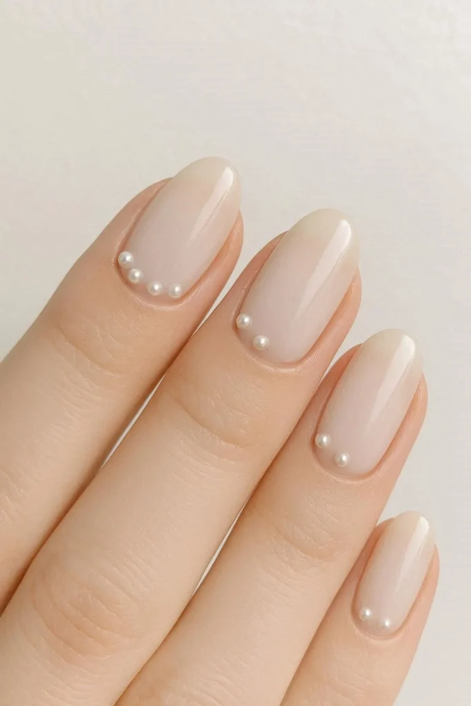 Milky nails with tiny flat back pearl accents placed along the cuticle on a creamy nude base