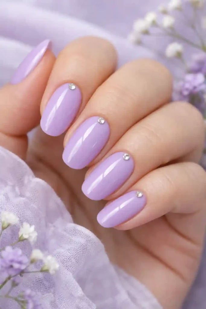 Pastel purple nails in soft wisteria shade with glossy finish and rhinestone detail