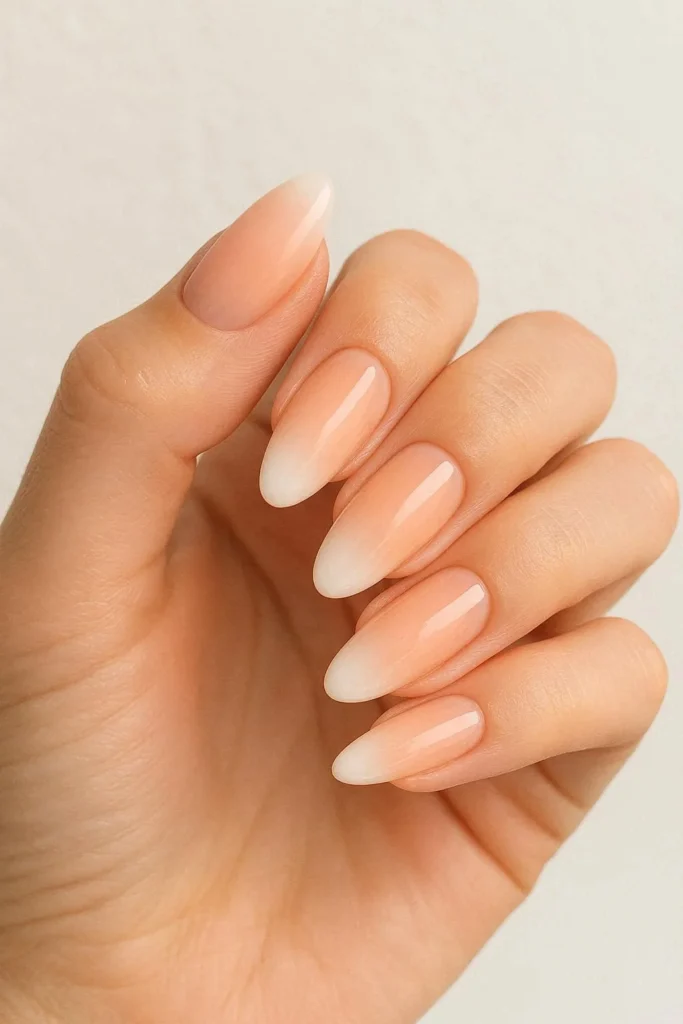 Peach ombre French fade nails blending soft peach into white tips on oval shaped nails with a glossy finish