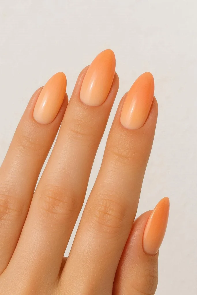 Peachy sunset ombre nails with a gradient from pale peach to warm coral on almond shaped nails