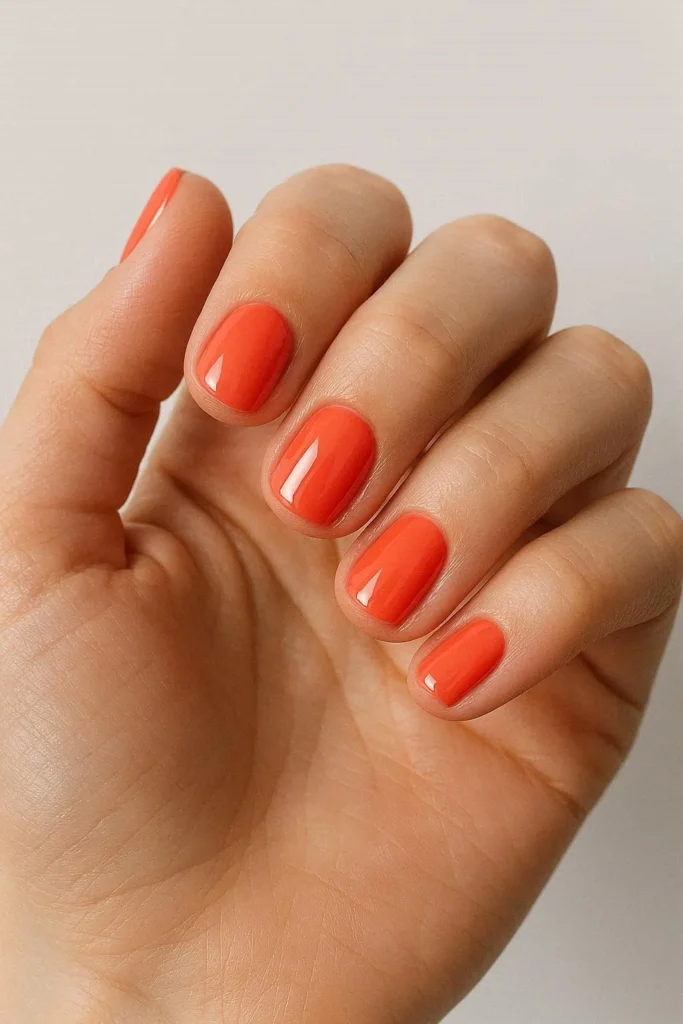 Short coral nails with a bold glossy finish on a square nail shape showing vibrant coral polish