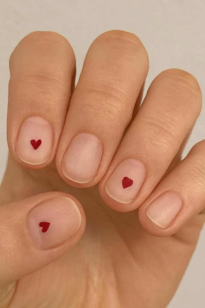 Small red heart accent nail on nude almond shape
