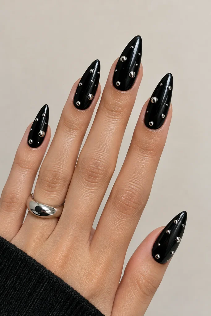 Glossy black stiletto nails featuring reflective chrome silver dots