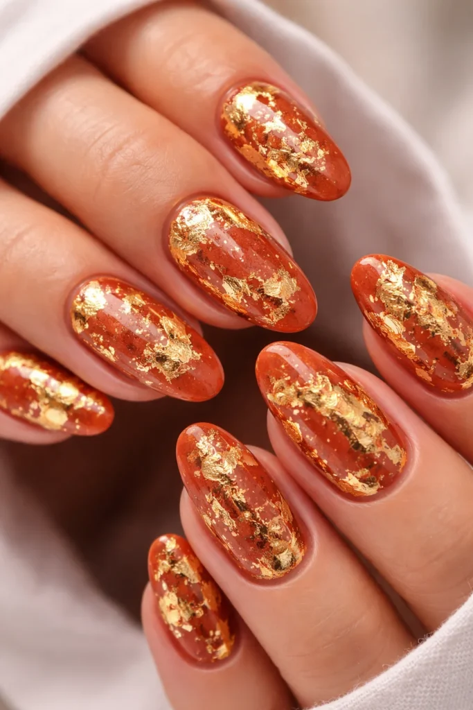 Gold foil Leo nails with abstract metallic detail on terracotta base