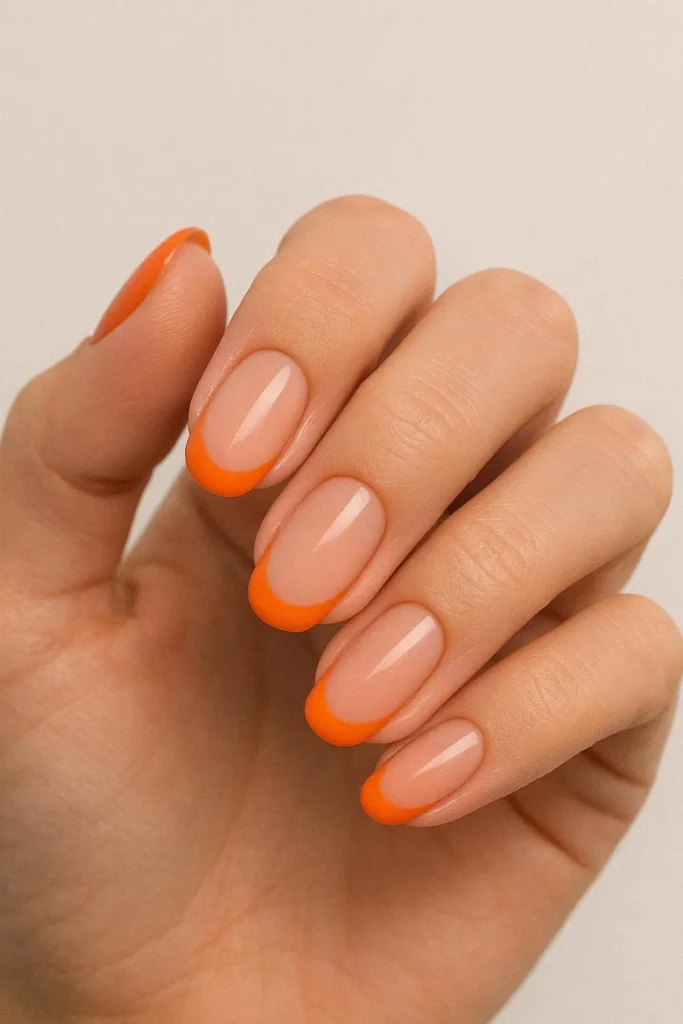 Nude nails with bold orange French tips for summer style