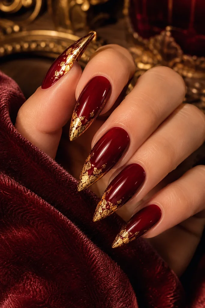 Deep red pointy nails decorated with gold foil near the tip