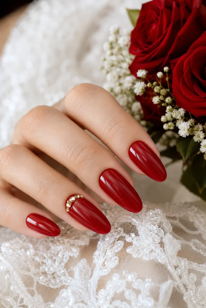 Soft red almond nails with gold rhinestone accents