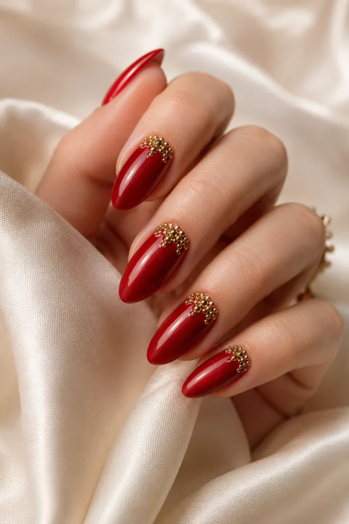 Red nails decorated with gold bead accents.