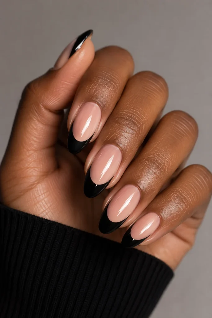 Nude almond nails with sleek black French tip outlines.