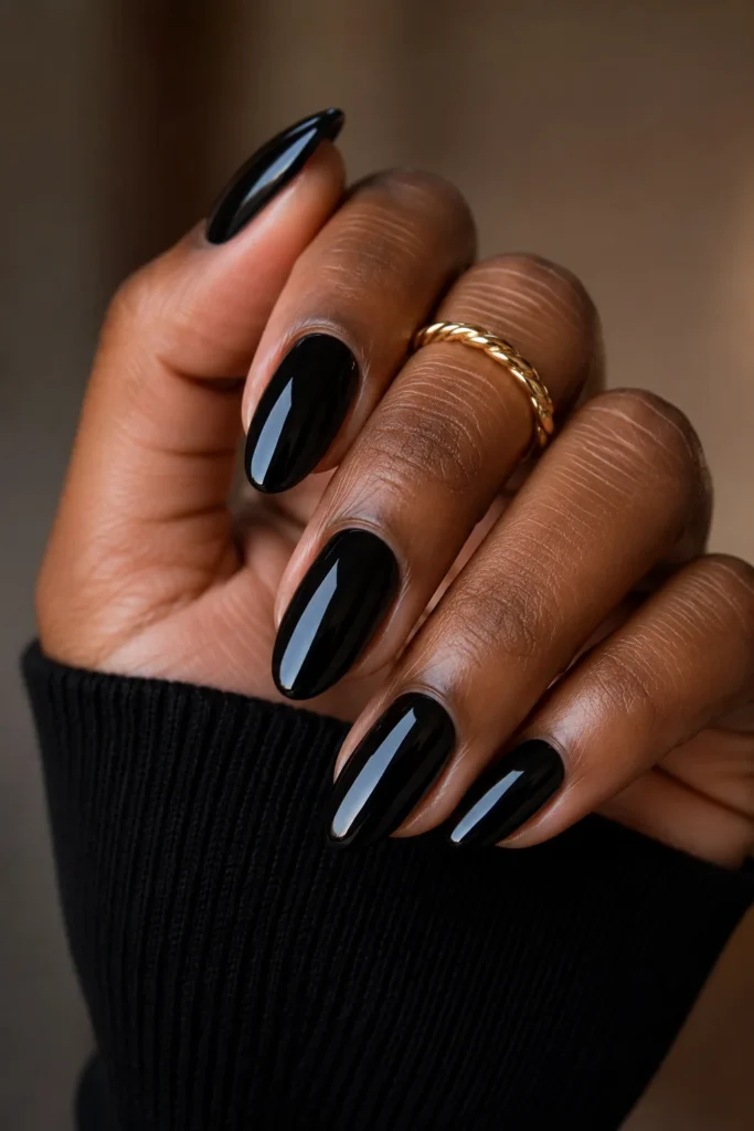 Simple glossy black almond nails paired with a gold ring.