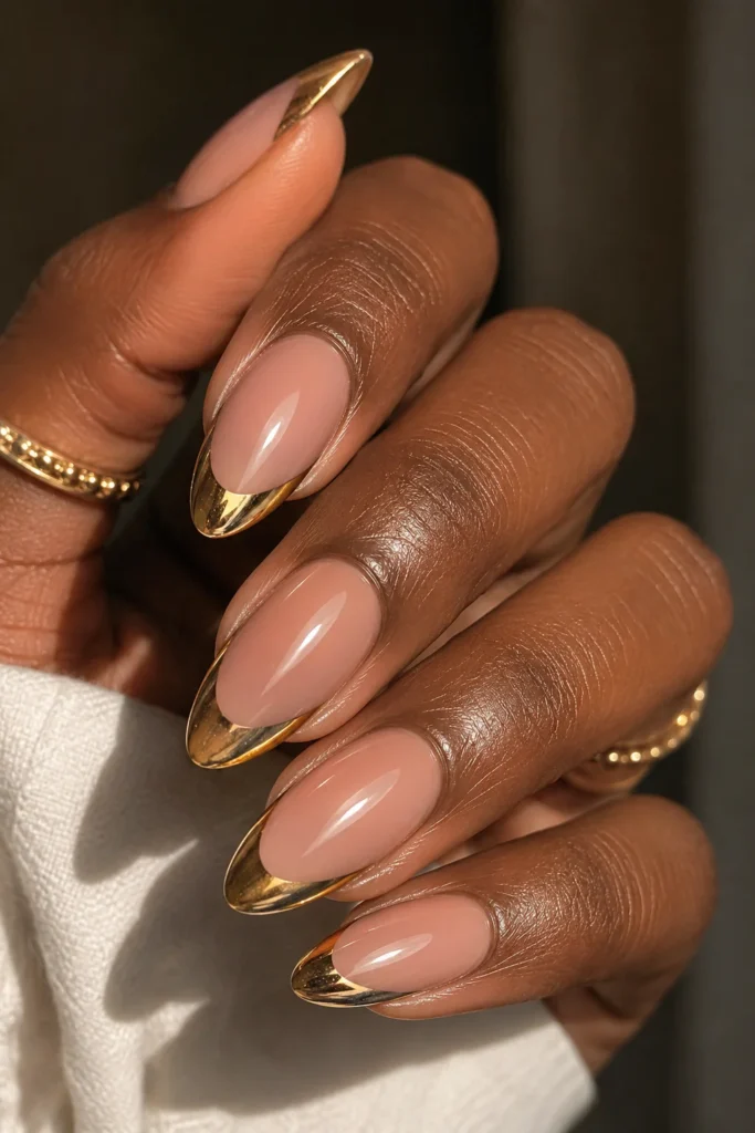 Gold chrome French tip almond nails on nude base, deep skin tone