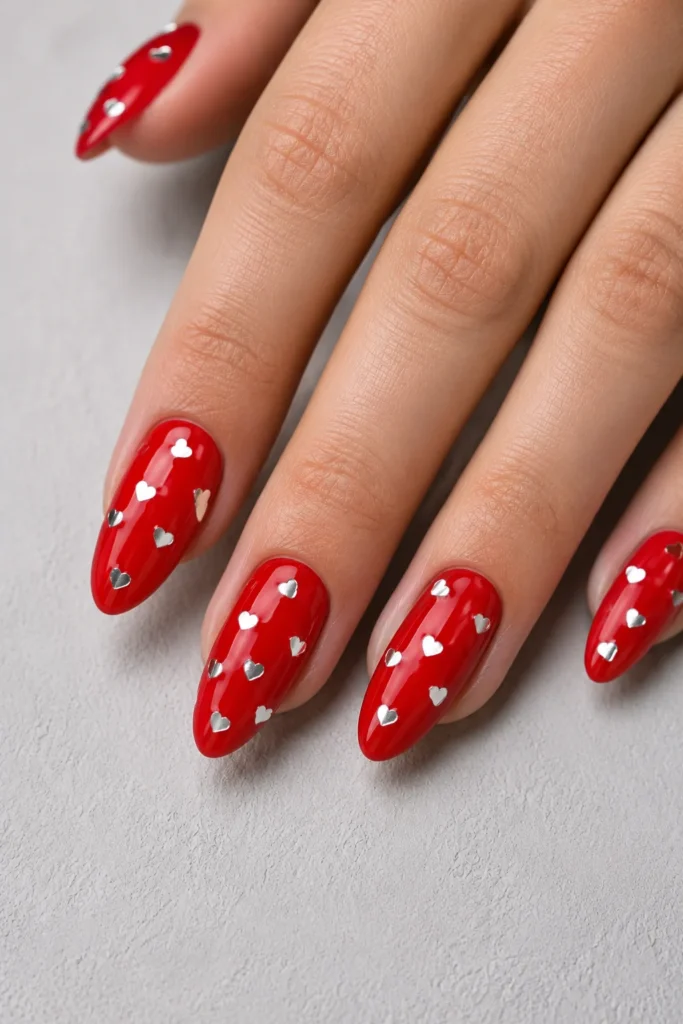 Glossy red nails decorated with tiny silver heart confetti