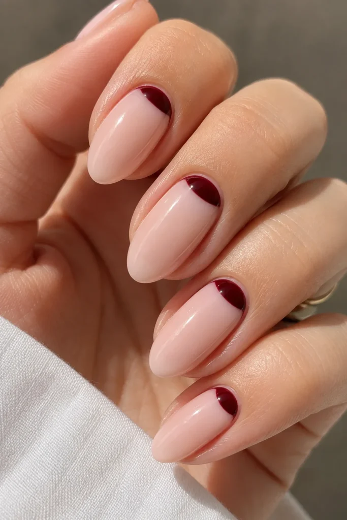 Oval nails with a burgundy half-moon shape painted at the cuticle