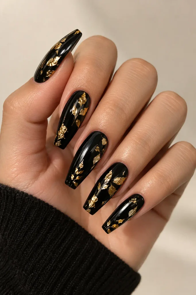 Glossy black nails decorated with scattered golden foil leaves