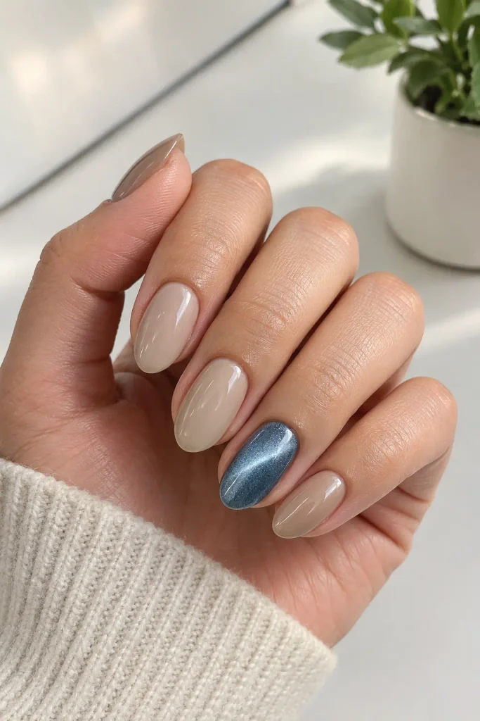 Neutral beige nails featuring one shimmering blue magnetic accent
