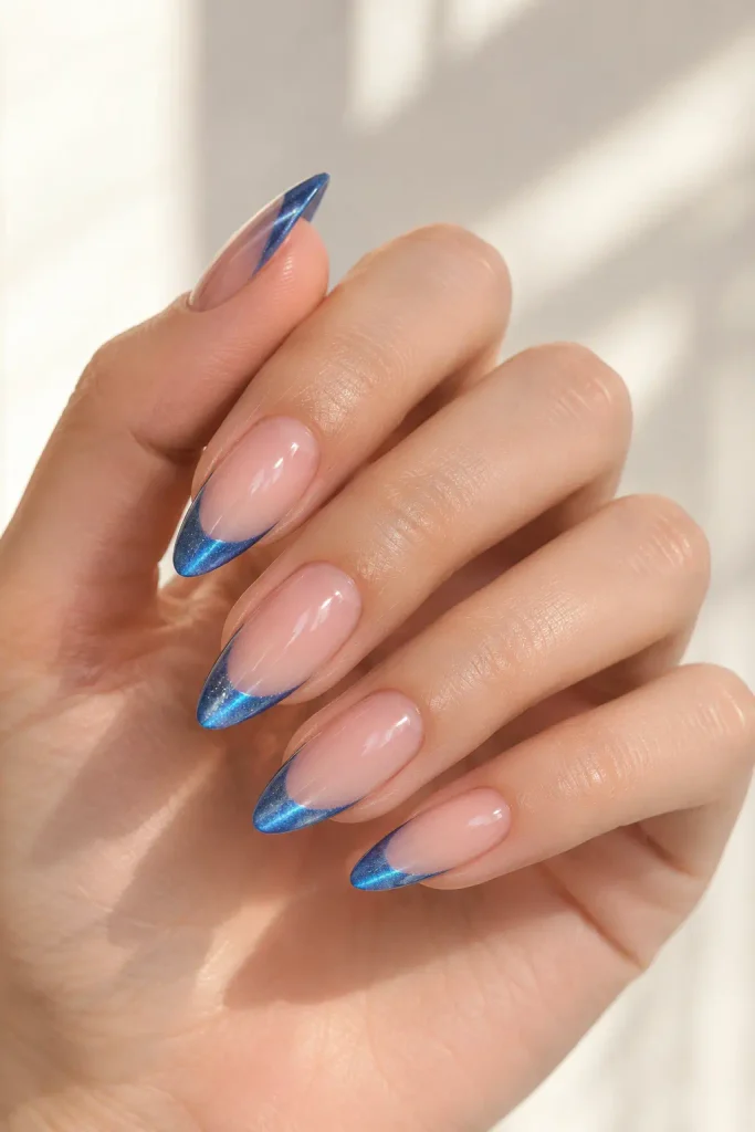 Sheer nude almond nails with shimmering blue magnetic French tips