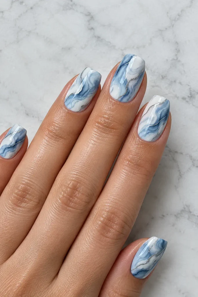 Medium blue and white marble nails with fine silver veins and glossy polish.