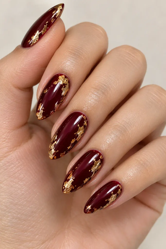 Deep burgundy nails accented with shimmering gold foil flakes