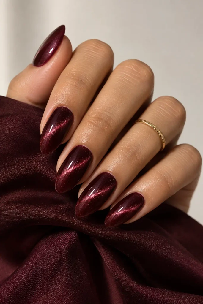 Medium almond nails featuring deep burgundy velvet magnetic shimmer polish