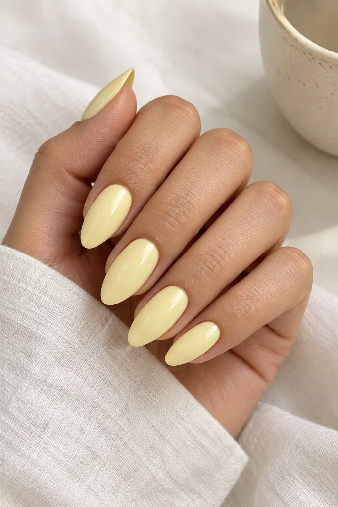 Medium almond acrylic nails in a soft milky butter yellow with a glossy finish.