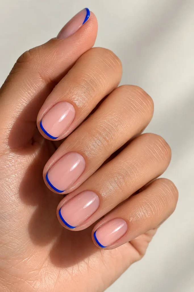 Short squoval wedding nails with sheer pink bases and thin cobalt blue French tips.