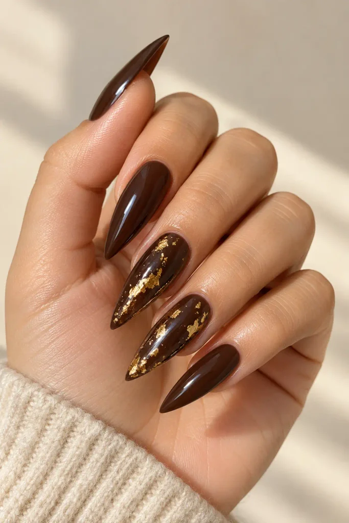 Espresso brown stiletto nails decorated with delicate gold foil.