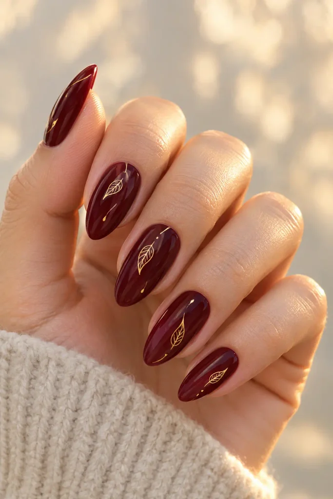 Burgundy wine nails featuring delicate golden falling leaf outlines